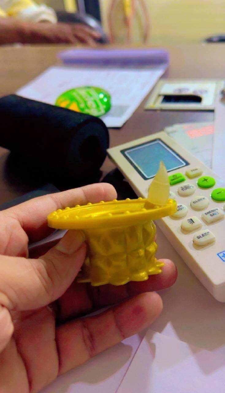 Hand holding yellow LED water pouring diya light with small flame detail near calculator and papers